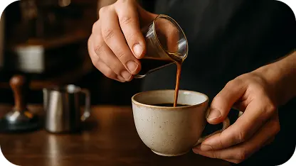Barista pouring fresh coffee from a small pot into a ceramic cup